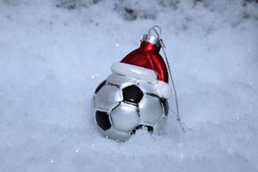 Silver and black soccer ball with the red and white Christmas hat, as decoration, among the beautiful snow