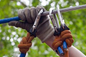 carabiners and climber's hand on a rope at blurred background with green plants