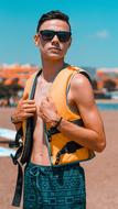 Young guy with sunglasses and orange vest, on the sandy beach
