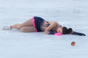 Figure skater girl lying on the ice near the colorful apple
