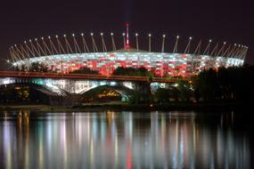 Warsaw national stadium is reflected in the river at night