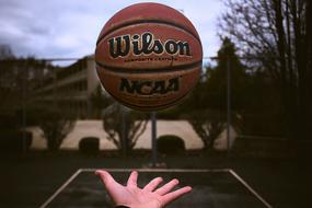 Brown, black and gold "Wilson" basketball, above the hand, on the court