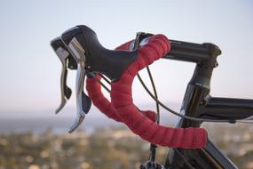 Close-up of the black, red and metallic handlebar of the racing bike, at blurred background with the shore