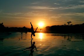 man stands on his hand on the beach against the background of sunset