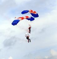 People, doing skydiving, with the colorful parachutes, at blue sky with white clouds on background