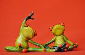 two frog figurines doing yoga on an orange background
