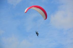 People, doing paragliding with the bi-place, red and white parachute, in the blue sky with clouds