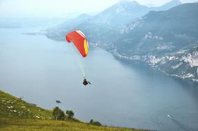 Person, doing paragliding on the colorful parachute, above the beautiful Garda Lake, and mountains, in Malcesine, Italy