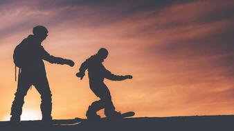 silhouettes of two snowboarders at sunset