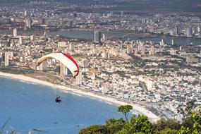 Person, doing paragliding on the red and white parachute, above the water, near the colorful city