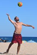 Man, playing beach volleyball, with the colorful ball, on the sandy beach