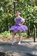 Girl ballerina in violet ballet tutu among the green trees