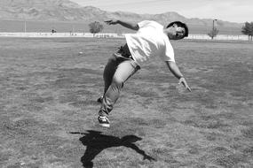 Black and white photo of the person, jumping above the grass on the shore, near the mountains in America