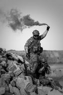Black and white photo with the soldier with the smoke, on the rocks, in the desert