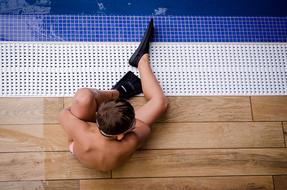 Child boy in equipment, sitting on the wet side of the pool