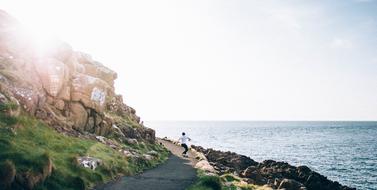 the guy walks along the road on the rock near the sea