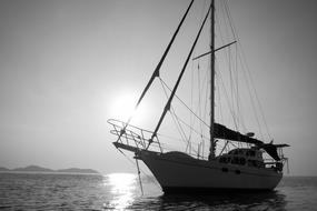 Black and white photo of the beautiful waterscape, in sunlight, with the sailing boat, and mountains on background