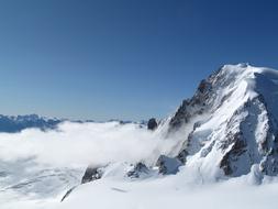 Beautiful, snowy, rocky mountain, among the white clouds, at blue sky on background