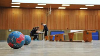 Colorful handballs on the floor and people at the table, in the building with lights