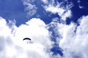 Paraglider high at blue sky background with white clouds