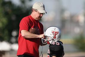 Coach helping with helmet to Football player of Youth League