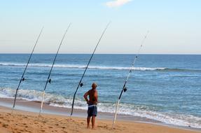 Surf fisherman, on the sandy beach, with the fishing poles, near the ocean, with the waves