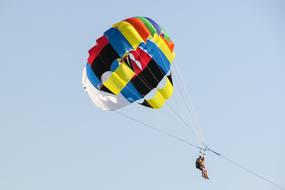 man flies on colored parachute in the sky