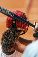 Back view of a softball girl player with curly hair, holding the bat
