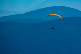 Paraglider flying beneath yellow wing at blue mountain landscape