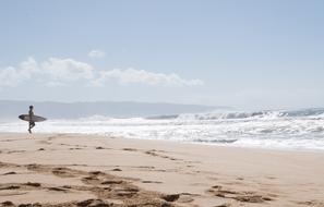 a man with a surfboard walks on the beach