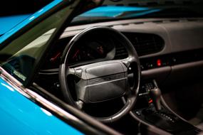 Black interior of the beautiful, shiny, blue Porsche 911 car, with the steering wheel and dashboard