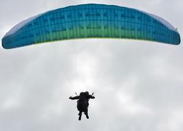 a man with a blue parachute under gray clouds