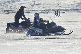 People in helmets, on the snowmobiles, on the snow, on the beautiful mountains in winter