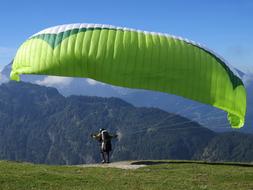 athlete on a green paraglider against the backdrop of mountains