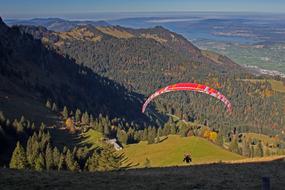 Person, doing paragliding on the red and white parachute, above the colorful and beautiful mountains