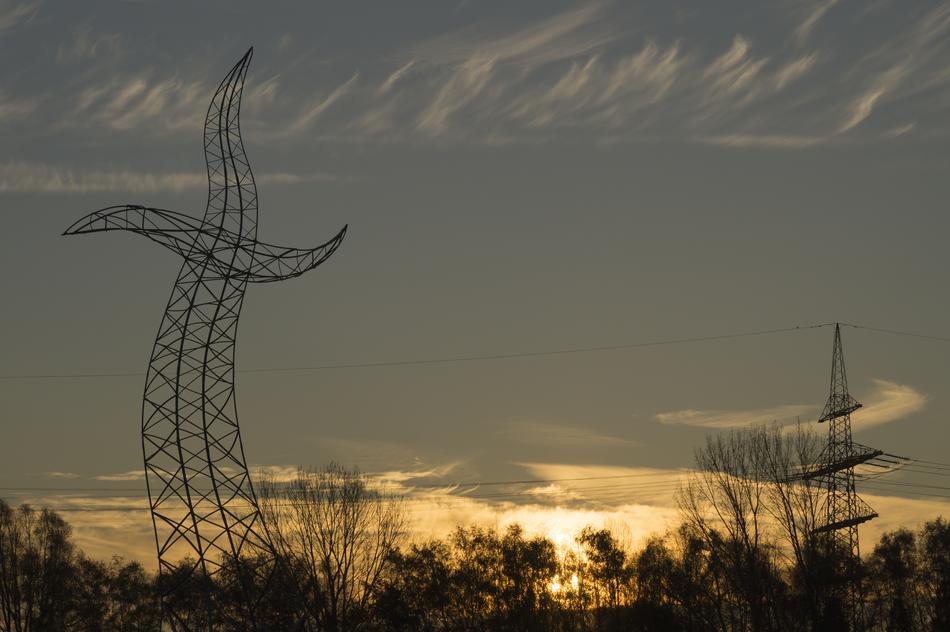 Silhouette of the dancing power lines, with the wires, above the beautiful landscape with the trees, at colorful sunrise in the clouds