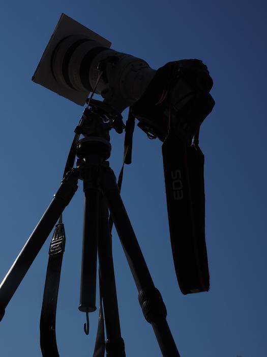 Silhouette of the black camera, on the tripod, in light, at blue sky on background