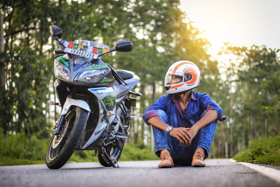 asian man in helmet sits on road beside of motorcycle