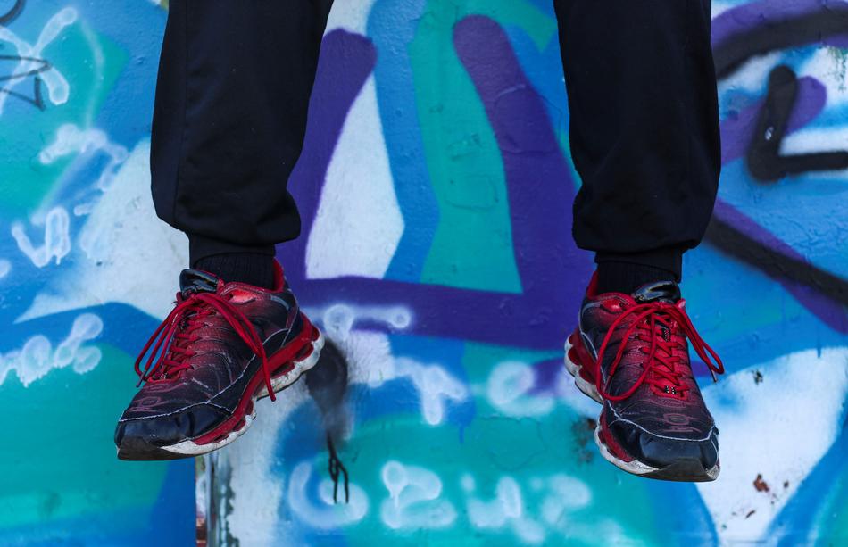 legs in sneakers and sweatpants dangle near the wall with graffiti