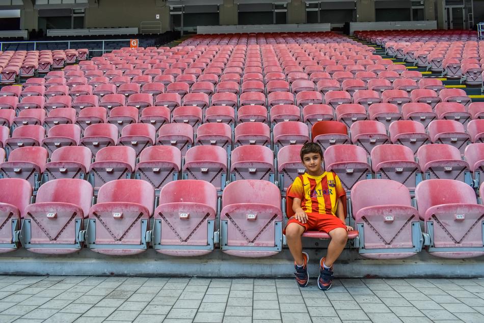 Child boy in red and yellow uniform, sitting on the red seat in the stadium