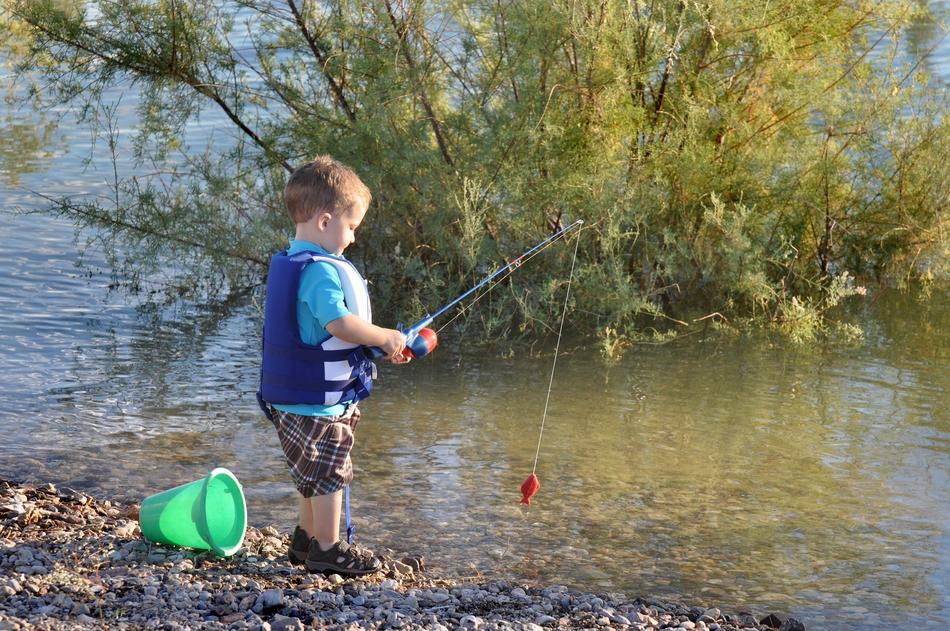 Child fishing on the beautiful shore with stones and green plants
