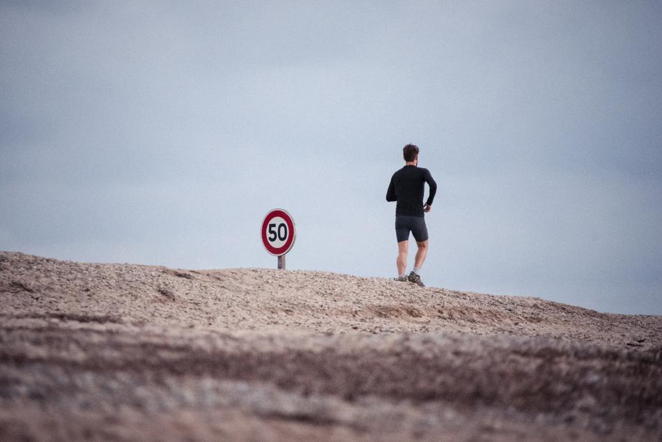 Male jogging on the landscape with the red, white and black '50' speed limit, under the cloudy sky