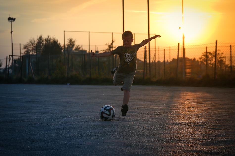 Boy, playing football on the court, at beautiful and colorful sunset