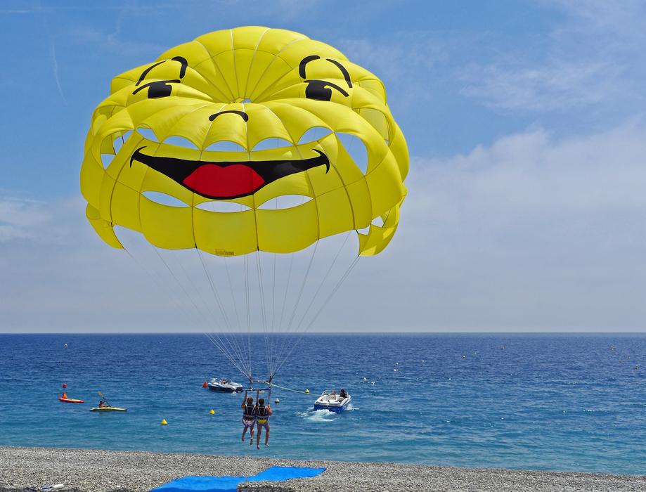 People, doing parasailing, on the colorful, cute parachute, with the smiley, near the water