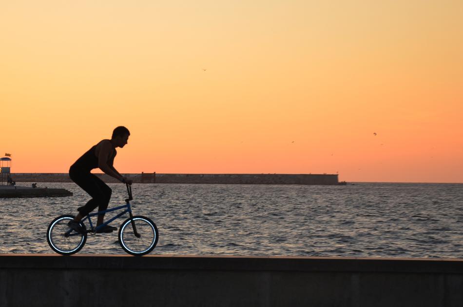 Silhouette of a person on the bike with turquoise wheels, on the coast, at beautiful and colorful, gradient sunset in Crimea