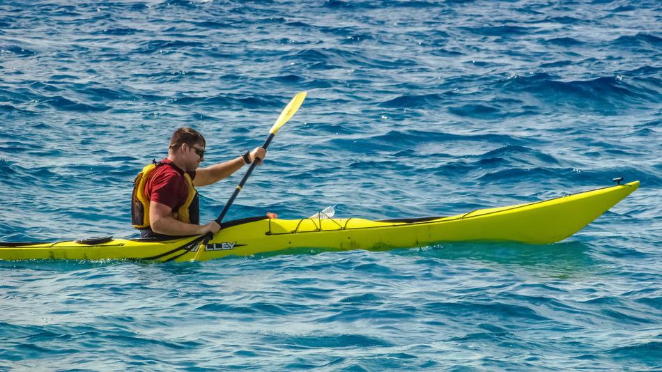 Man, kayaking on the yellow board, among the green and blue water