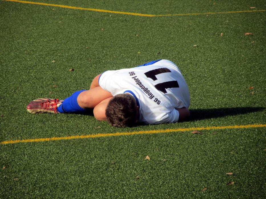 Football player, with the injury, laying on the green field, with the yellow line