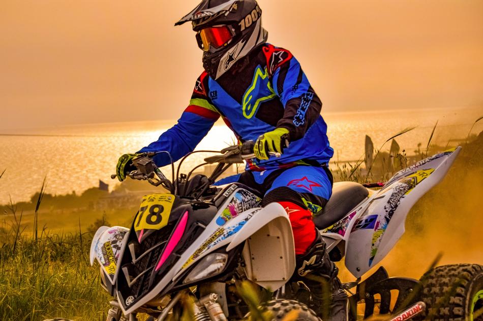 Colorful person on the quad, on the motocross competition, on the beautiful and colorful coast, at sunset