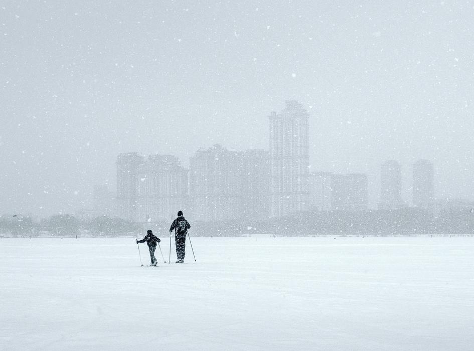 a child with a parent is skiing in a snowstorm in winter