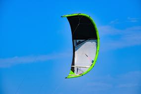 Green, gray and black parachute for kitesurfing at blue sky background